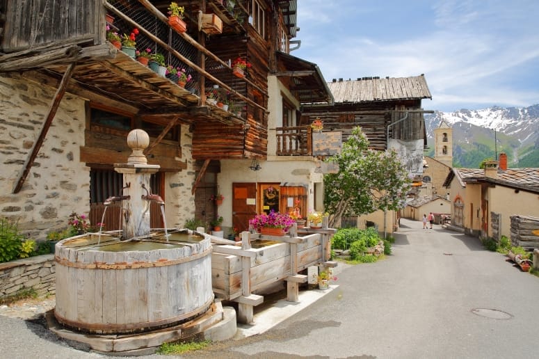 Fontaine en bois rustique dans un village alpin fleuri avec vue sur les montagnes